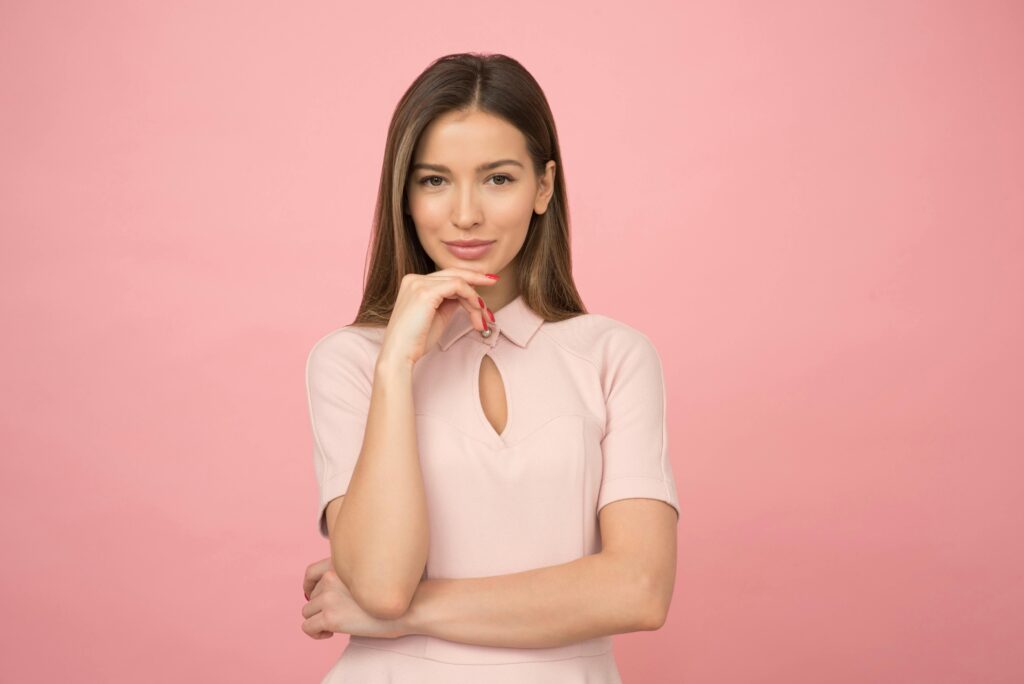 Portrait of a young woman posing elegantly in a studio with a pink background.